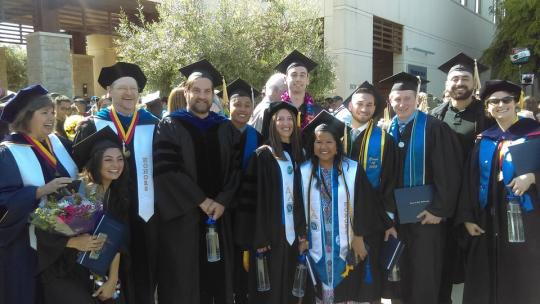 Smiling people wearing graduation regalia.